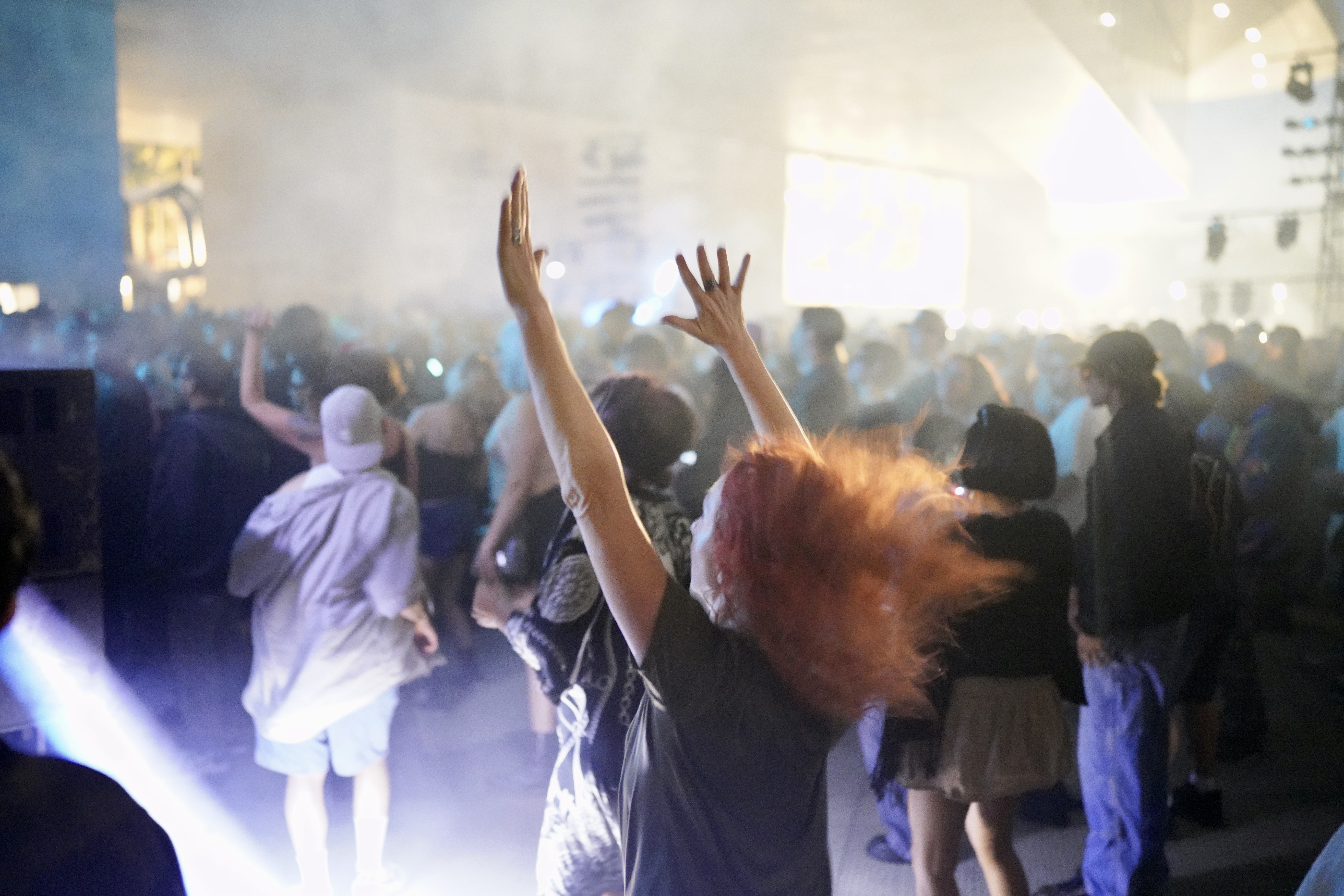 woman with red hair raising her arms up as her hair floats back. She's in the midst of a large crowd