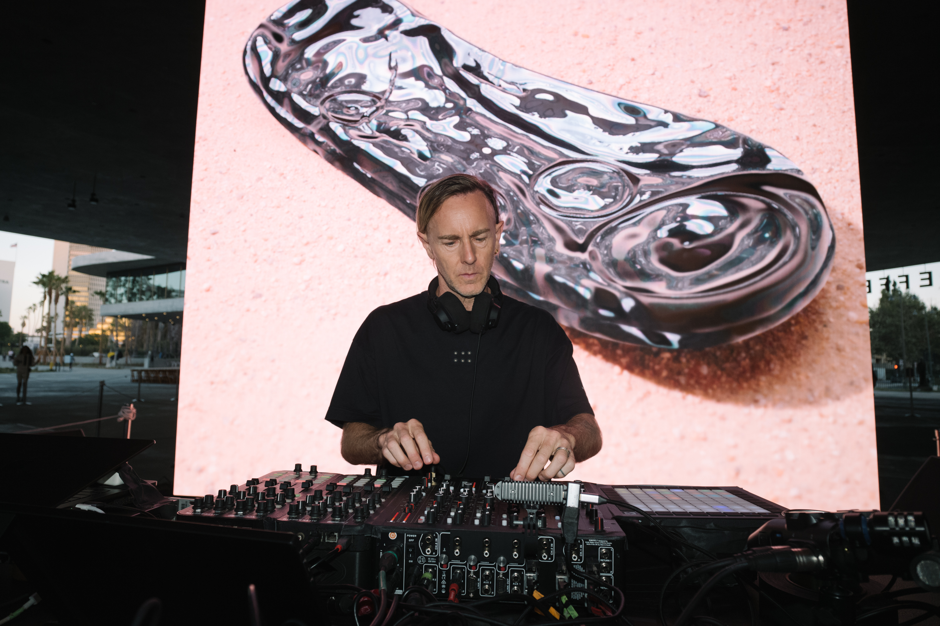 Close up image of DJ Richie Hawtin playing music with a large screen of a shoe in a desert lanscape