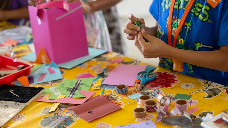 children off screen working on artwork at table with paper and tape