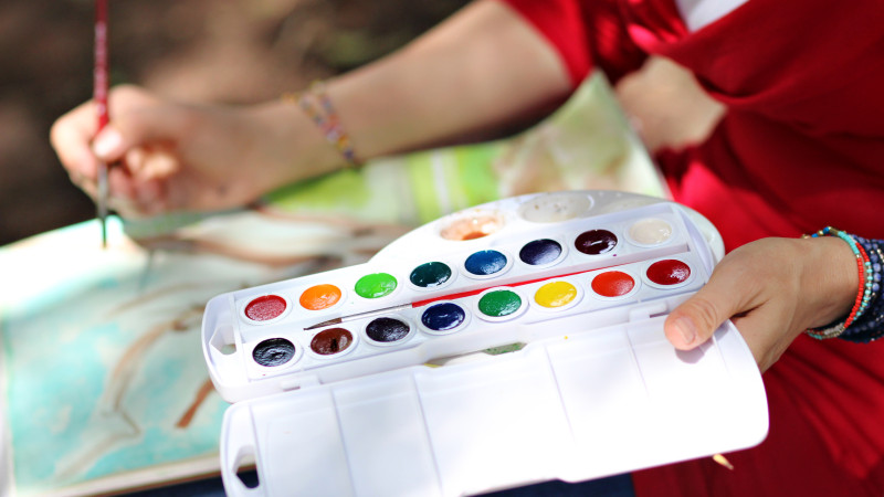 image of person holding watercolor palette while working on a watercolor painting