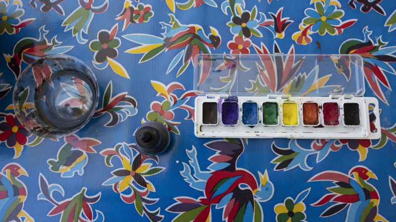 watercolor paint palette and water bowl on colorful tablecloth