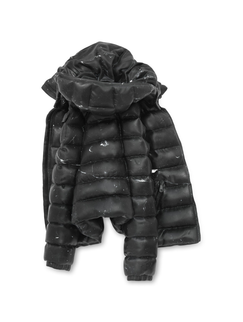 Black quilted puffer jacket with a large hood, crumpled and laid flat, showing scattered scuff marks and wear across the fabric.
