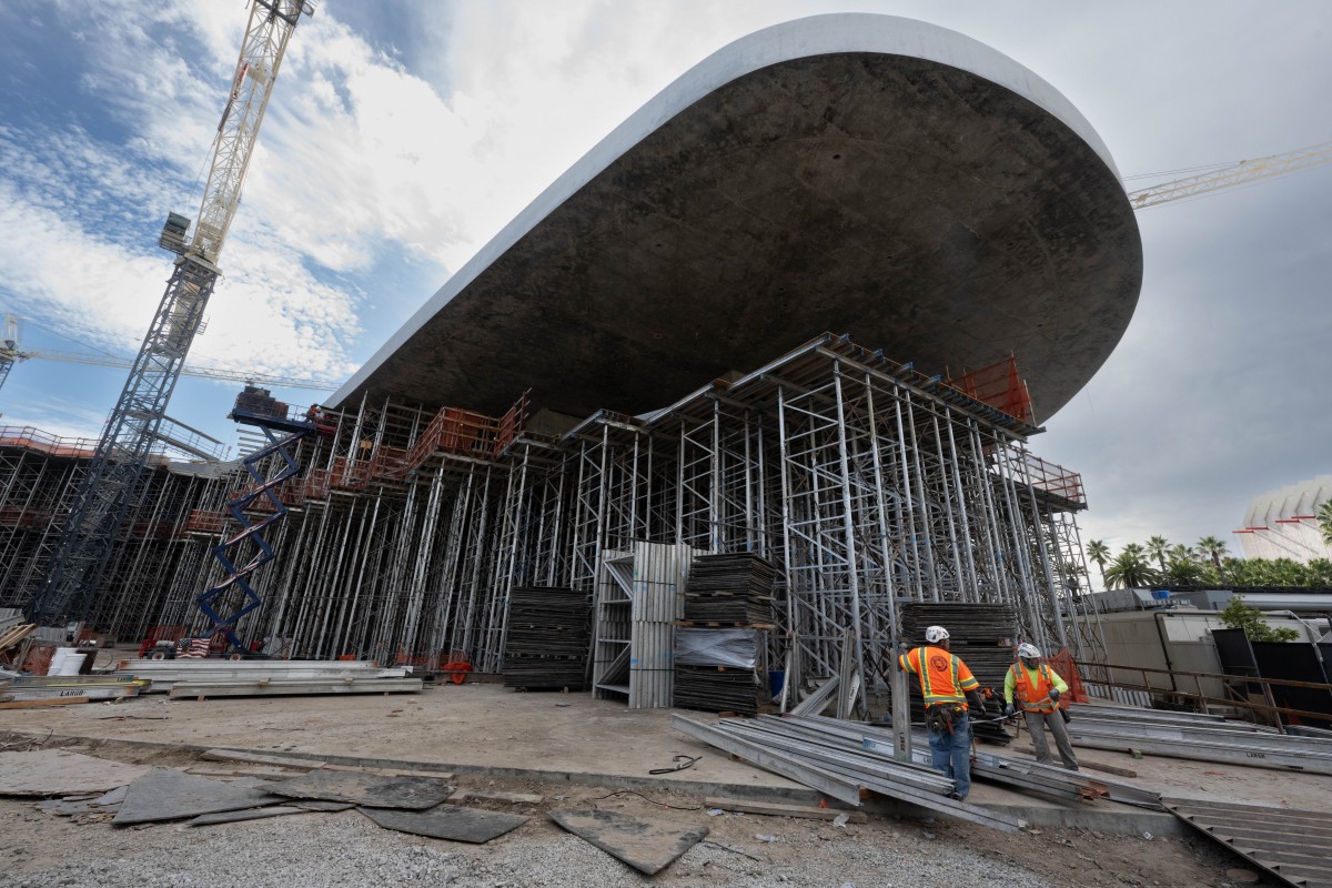 Curved gray building cantilevered over scaffolding on a construction site