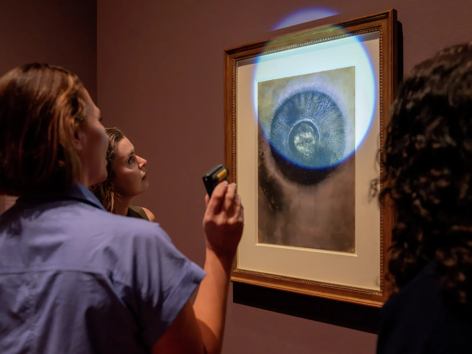 <p>Michelle Sullivan, Lucia Elledge, and Danielle Canter observe Odilon Redon’s Head within an Aureole, featured in the exhibition Odilon Redon: Otherworldly Visions at the Getty Center. Image: Getty Museum. © J. Paul Getty Trust</p>